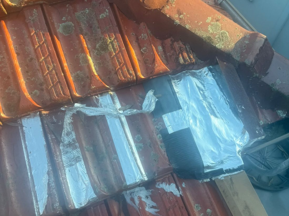 Strips of foil tape and smeared sealant stuck over old terracotta roof tiles as a previous leak repair