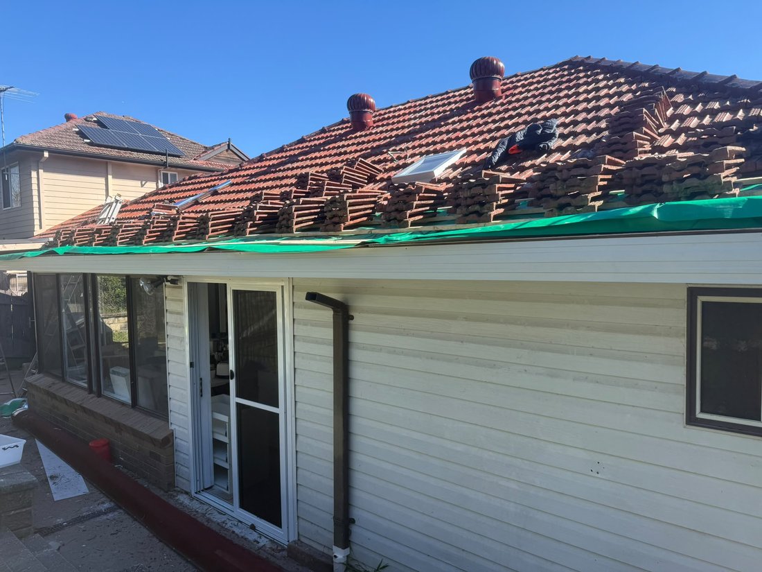 Roof tiles lifted and stacked in rows across a roof during a sarking retrofit